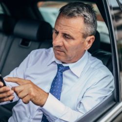 Man inside his car using his phone to read about title loans online direct deposit